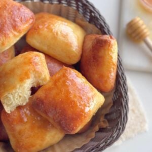 No-knead honey butter dinner rolls baked until golden with one roll torn open showing the fluffy interior.