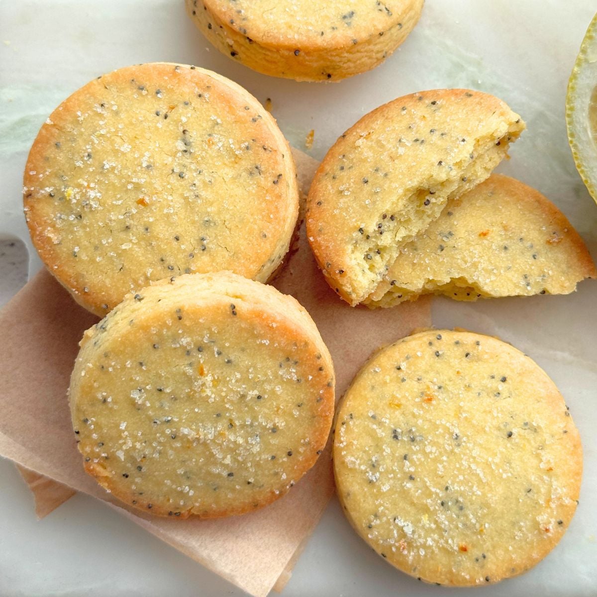 Lemon poppy seed cookies on parchment with cookie broken in half to show texture