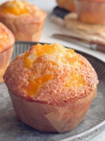 Peach muffins topped with diced peaches and sugar, baked with fresh or canned peaches.