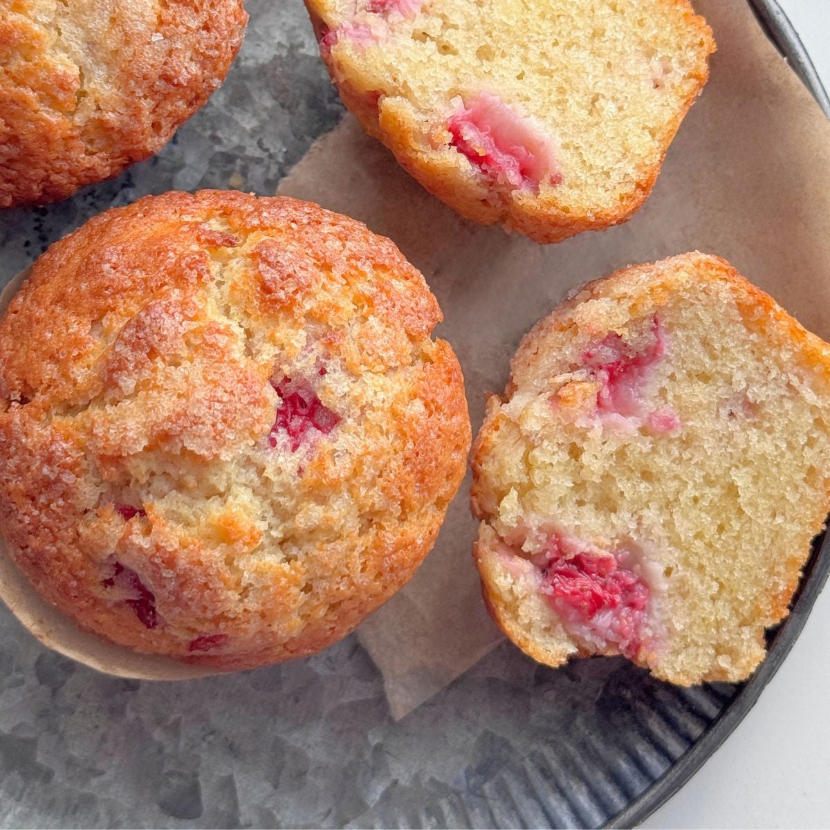 Baked strawberry muffins with one cut open to show the light texture and juicy strawberries inside.